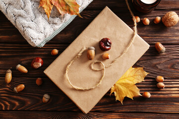 Book with autumn leaf as bookmark, acorns, scented candle and warm sweaters on wooden table, flat lay