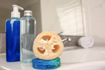 Loofah sponge and cosmetic products on sink in bathroom, space for text
