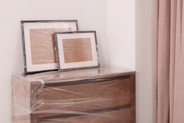 Picture frames and chest of drawers wrapped in stretch film indoors