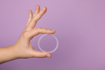 Woman holding diaphragm vaginal contraceptive ring on lilac background, closeup. Space for text