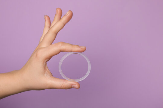 Woman holding diaphragm vaginal contraceptive ring on lilac background, closeup. Space for text