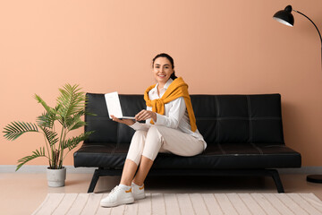 Young woman using laptop on black couch near beige wall