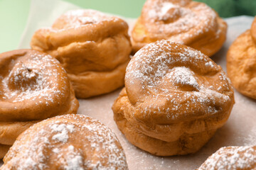 Delicious profiteroles with powdered sugar on parchment paper, closeup