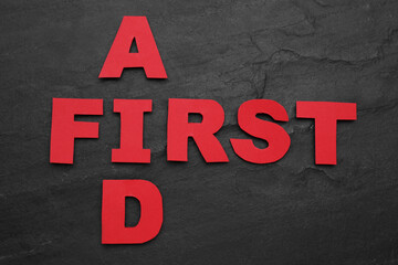 Words First Aid made of red letters on black table, flat lay