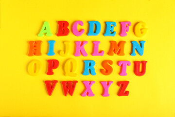 Plastic magnetic letters on yellow background, flat lay. Alphabetical order