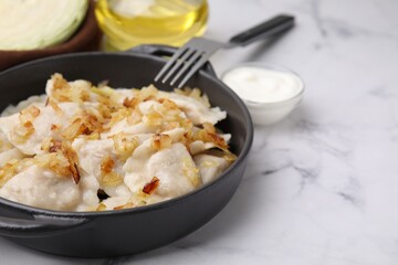 Cooked dumplings (varenyky) with tasty filling and fried onions on white marble table, closeup