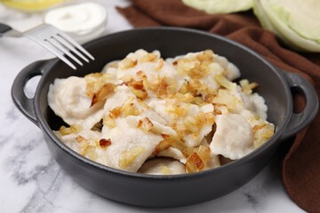 Cooked dumplings (varenyky) with tasty filling and fried onions on white marble table, closeup