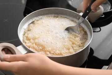 Woman cooking tasty pasta on stove, closeup