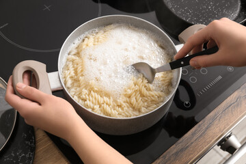 Woman cooking tasty pasta on stove in kitchen, closeup
