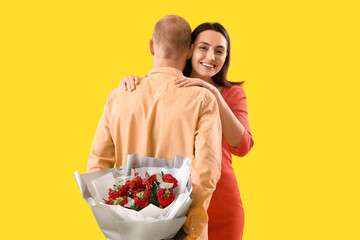 Young couple with bouquet of flowers on yellow background. Valentine's Day celebration