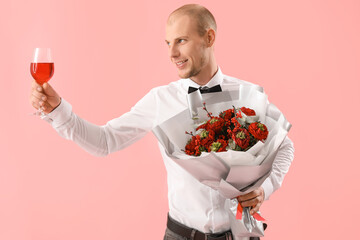 Young man with glass of wine and flowers on pink background. Valentine's Day celebration