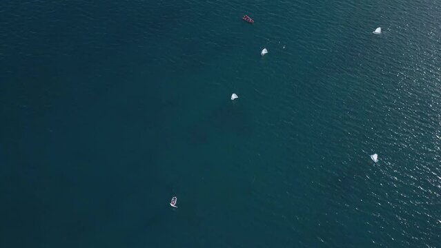 Junior sailors sport competition. Junior yacht club regatta in the open sea, teachers boat make a turn. Junior training course on sailboats. Aerial drone video slow motion footage.