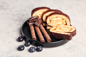 Plate with pieces of tasty sponge cake roll, chocolate, waffle rolls and blueberry on grunge background