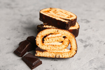 Pieces of tasty sponge cake roll and chocolate on grunge background