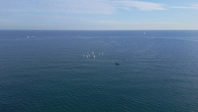 Camera approaching a bunch of boats in open sea Junior sailors sport competition. Junior yacht club regatta in the open sea. Junior training course on sailboats. Aerial drone video. 