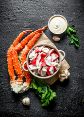 Crab meat in bowl on paper with greens, sauce and garlic.