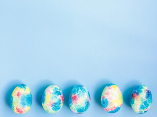 Colorful handmade Easter eggs painted like Earth on blue paper background with copy space for your Easter text message. Minimal happy Easter holiday conceprt. Top view flat lay, border frame