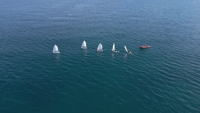 Junior sailors sport competition. Junior yacht club regatta in the open sea, boats make a turn. Junior training course on sailboats. Aerial drone video side view. 