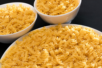 Uncooked Fusilli Pasta Lying on White Plate on Black Background. Raw and Dry Macaroni. Unhealthy and Fat Food