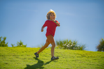 Cute boy running on green grass and blue sky. Little runners outdoors in summer nature. Sporty child running in a park. Outdoor sports and fitness for children.