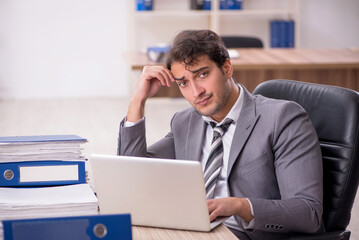 Fototapeta premium Young male employee unhappy with excessive work in the office