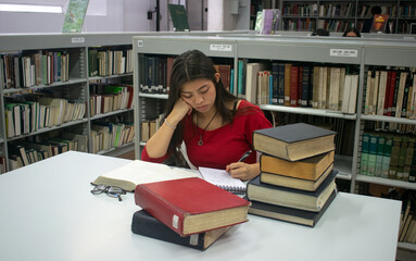 Chica universitaria de blusa roja escribiendo y estudiando en la biblioteca	