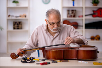 Old male repairman repairing musical instruments at workshop