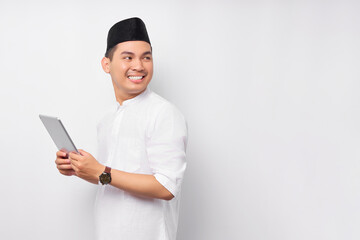 Smiling young Asian Muslim man holding digital tablet and looking at empty copy space isolated on white background. People religious Islam lifestyle concept. celebration Ramadan and ied Mubarak