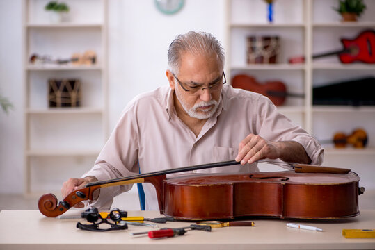 Old male repairman repairing musical instruments at workshop