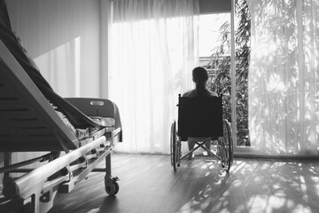 The woman sitting on wheelchair. She is see window with patient bed in hospital.disabled person...