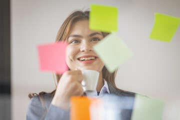Business Asian female employee with many conflicting priorities arranging sticky notes commenting...