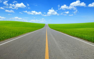 Strait tarmac road in slope grass field with blue sky background.