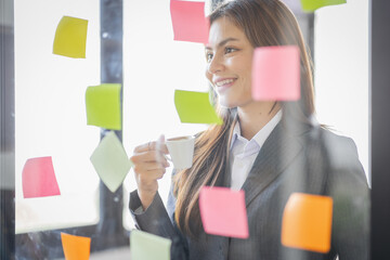 Business Asian female employee with many conflicting priorities arranging sticky notes commenting...