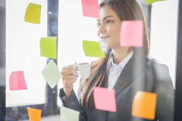Business Asian female employee with many conflicting priorities arranging sticky notes commenting and brainstorming on work priorities colleague in a modern office.