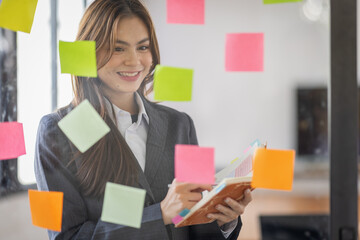 Business Asian female employee with many conflicting priorities arranging sticky notes commenting...