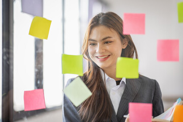 Business Asian female employee with many conflicting priorities arranging sticky notes commenting...