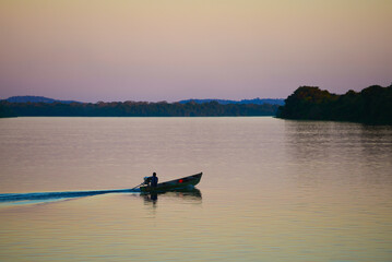 A boat at sunset on the rainforest-lined Guaporé-Itenez river, near the remote village of Cafetal, Beni Department, Bolivia, on the border with Rondonia state, Brazil