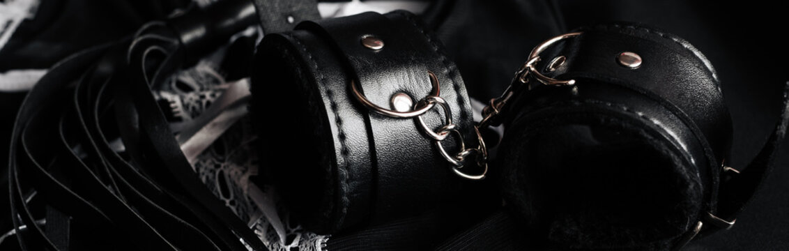 Leather handcuffs and whip for BDSM and maid costume for role-playing games. Sex toys for domination and submission. Panoramic wide horizontal photo for banner head cover