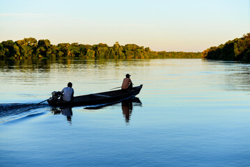 Two men on a boat at sunset on the rainforest-lined Guaporé-Itenez river, near the remote village...