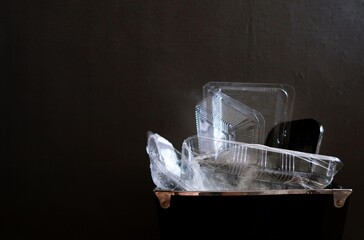 Single use plastic food containers in black trash can on dark wall background with copy space-  daily plastic waste in household raising global crisis. - obrazy, fototapety, plakaty