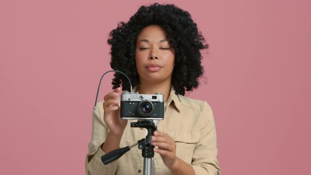 Professional female photographer capturing pictures with a dslr camera. Creative young woman smiling while using camera at studio background. Woman of color making shot on vintage retro film camera 4K