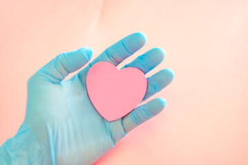 Male hands in blue medical gloves hold a pink heart symbol. Hands holding a pink heart.The gesture symbolizes of love. Help and volunteering, Insurance health care, pink love, Valentine day concept.