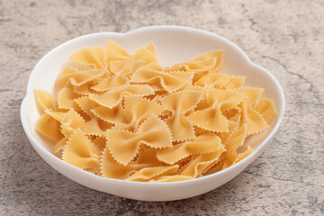 Raw macaroni in white cup on brown background