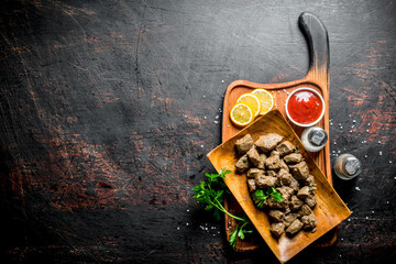 Pieces of cooked liver on a cutting Board with lemon, herbs and tomato sauce.