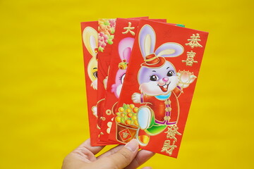 Theme red envelopes with rabbit, Chinese blessing words on yellow background for Chinese Lunar New Year. Hello 2023 year of rabbit. Imlek decoration.