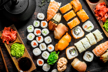 Different types of Japanese sushi, rolls and maki with sauce, wasabi and green tea in a teapot.