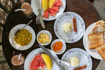 Traditional Sri Lankan breakfast with egg omelette, sausage, lentil curry, fruits, wood apple fresh, jam, butter and toast on terrace.