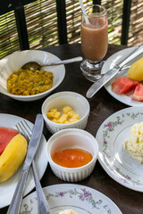 Traditional Sri Lankan breakfast with egg omelette, sausage, lentil curry, fruits, wood apple fresh, jam, butter and toast on terrace.