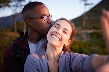 Interracial couple, kiss and smile for selfie, travel or love for adventure, journey or hiking together in nature. Happy man kissing woman smiling in happiness for photo moments, trip or traveling - obrazy, fototapety, plakaty