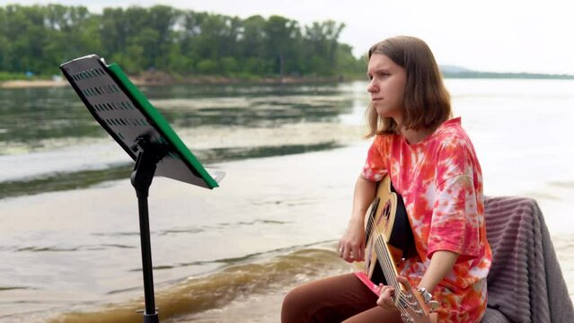 A young girl plays an acoustic guitar on the banks